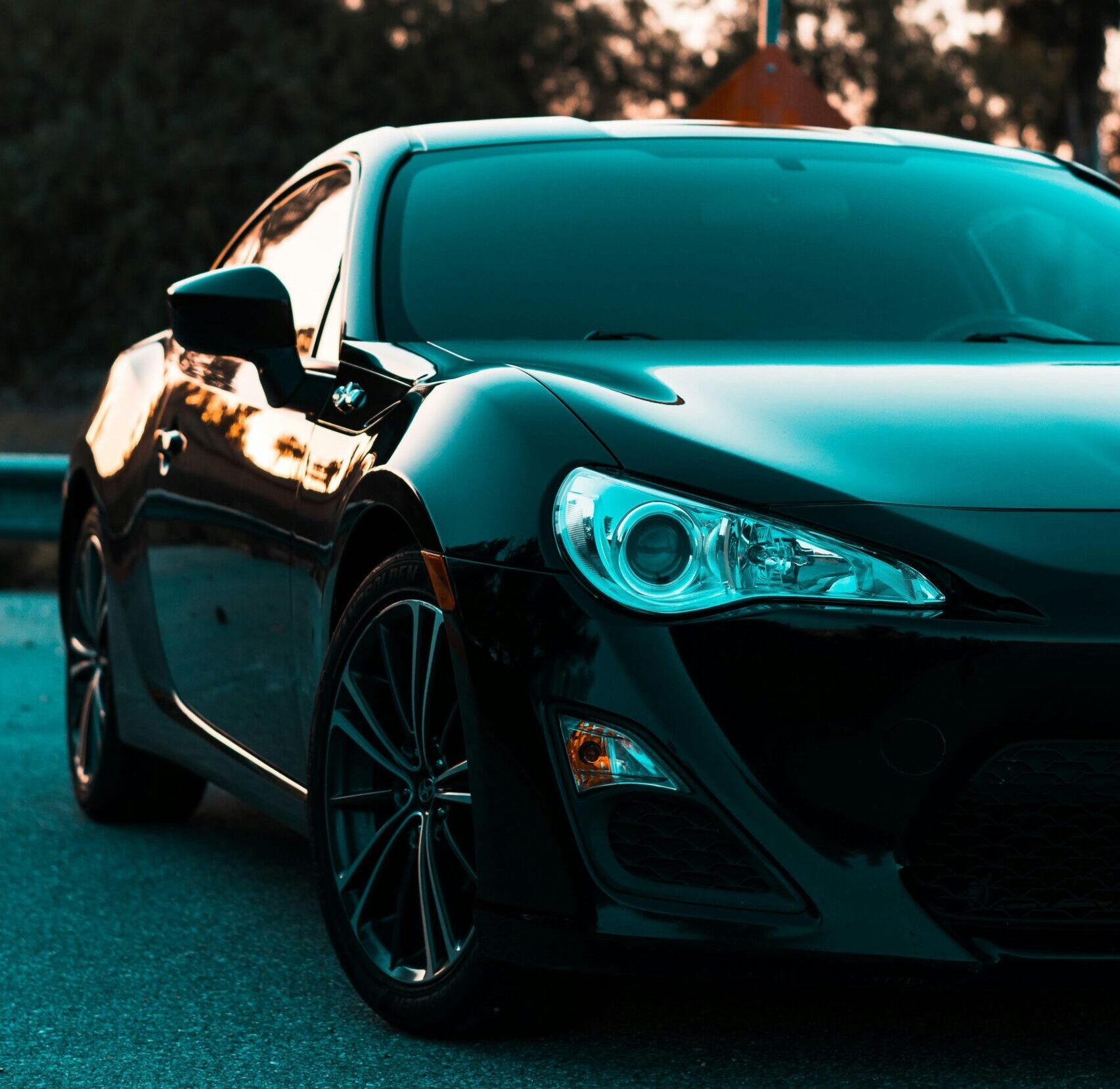 Stylish black luxury car parked near a road end sign, surrounded by lush greenery.