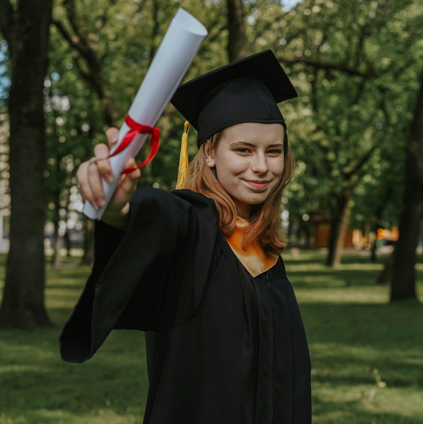 A proud female graduate holding a diploma in a green park setting.