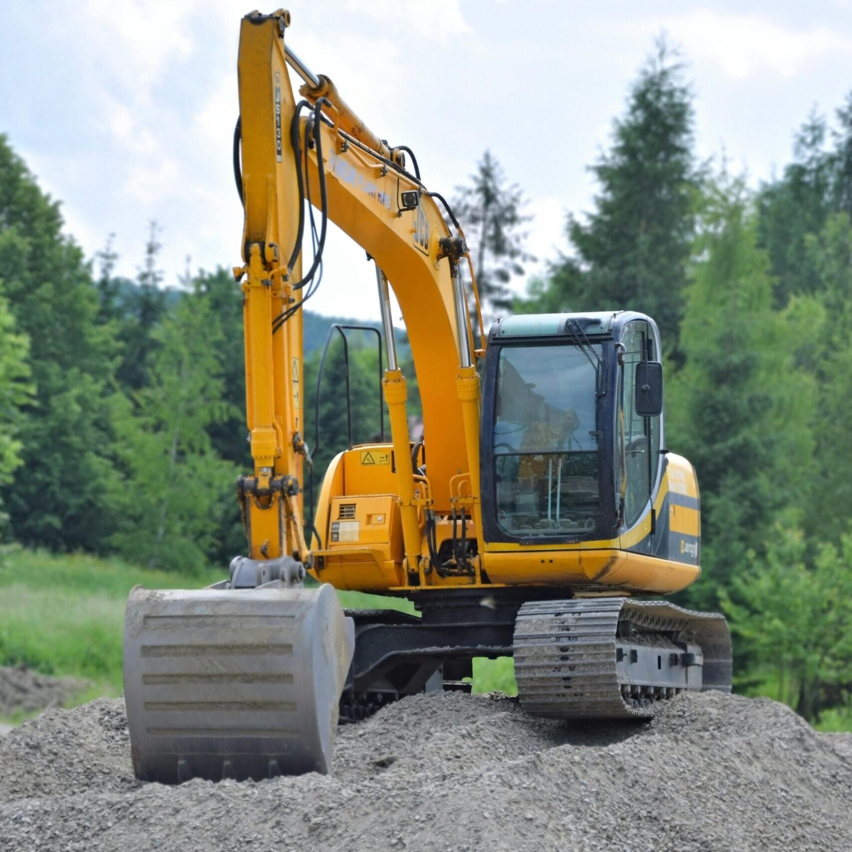 A yellow excavator on a pile of gravel in a lush, green forest setting in Poland.